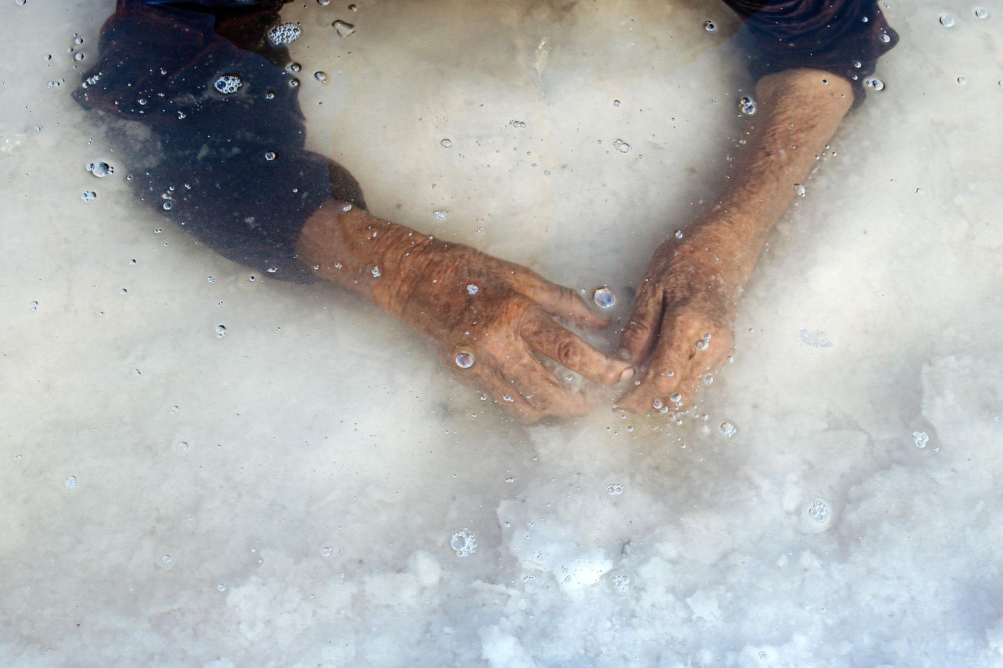 In das seichte Wasser des fast ausgetrockneten Urmia-Sees tauchen die Hände einer älteren Frau, es ist die Großmutter der Fotografin Solmaz Daryani. Die Haut ist vom Leben gezeichnet, der See vom Klimawandel. In das einst größte Binnengewässer des Irans hätte noch in den 1990er Jahren der Bodensee neunmal hineingepasst. Heute bleibt vielerorts nur eine kristalline Kruste und flaches Restwasser zurück. Die Geste der Großmutter ist unscheinbar und zugleich tief: ein Prüfen, Tasten, vielleicht ein Erinnern an Zeiten, in denen der See noch ein Ort des Badens, der Erholung und des Alltags war. Und so verbindet das Bild eine persönliche Geschichte mit einer ökologischen Tragödie