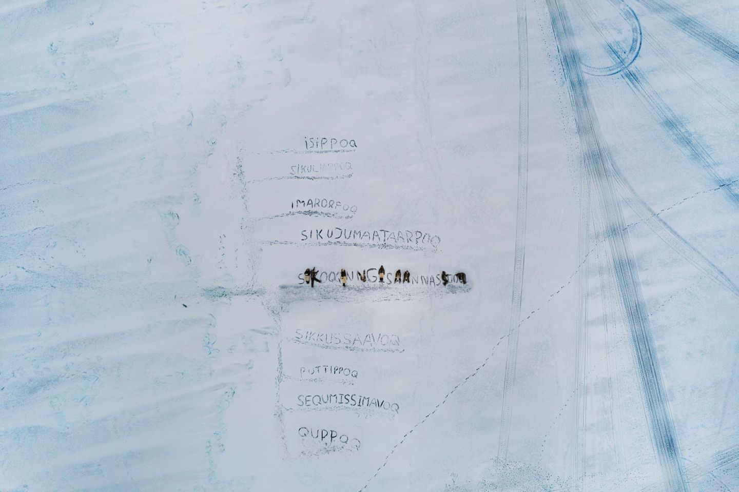 In Uummannaq, einer Siedlung im Nordwesten Grönlands, ritzen Kinder Worte ins Meereis. Die Begriffe stammen aus dem Kalaallisut, dem westgrönländischen Dialekt, der für seine Fähigkeit bekannt ist, komplexe Veränderungen in langen zusammengesetzten Wörtern zu fassen. Während das Eis früher monatelang als sichere Verkehrsfläche galt, wird es heute dünner, poröser, unberechenbarer. Die Kinder verwenden Sprache, um das Unfassbare zu vermessen: neue Begriffe für neues Wissen, neue Risiken, neue Gefühle. In diesem Bild werden das Schmelzen und die Unsicherheit sichtbar. Nicht durch Daten oder Karten. Dafür aber durch eine junge Generation, die versucht, einer verändernden Welt Bedeutung zu geben