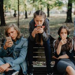 mehrere Kinder sitzen auf einer Bank und schauen auf ihr Telefon