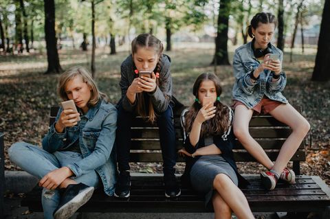 mehrere Kinder sitzen auf einer Bank und schauen auf ihr Telefon