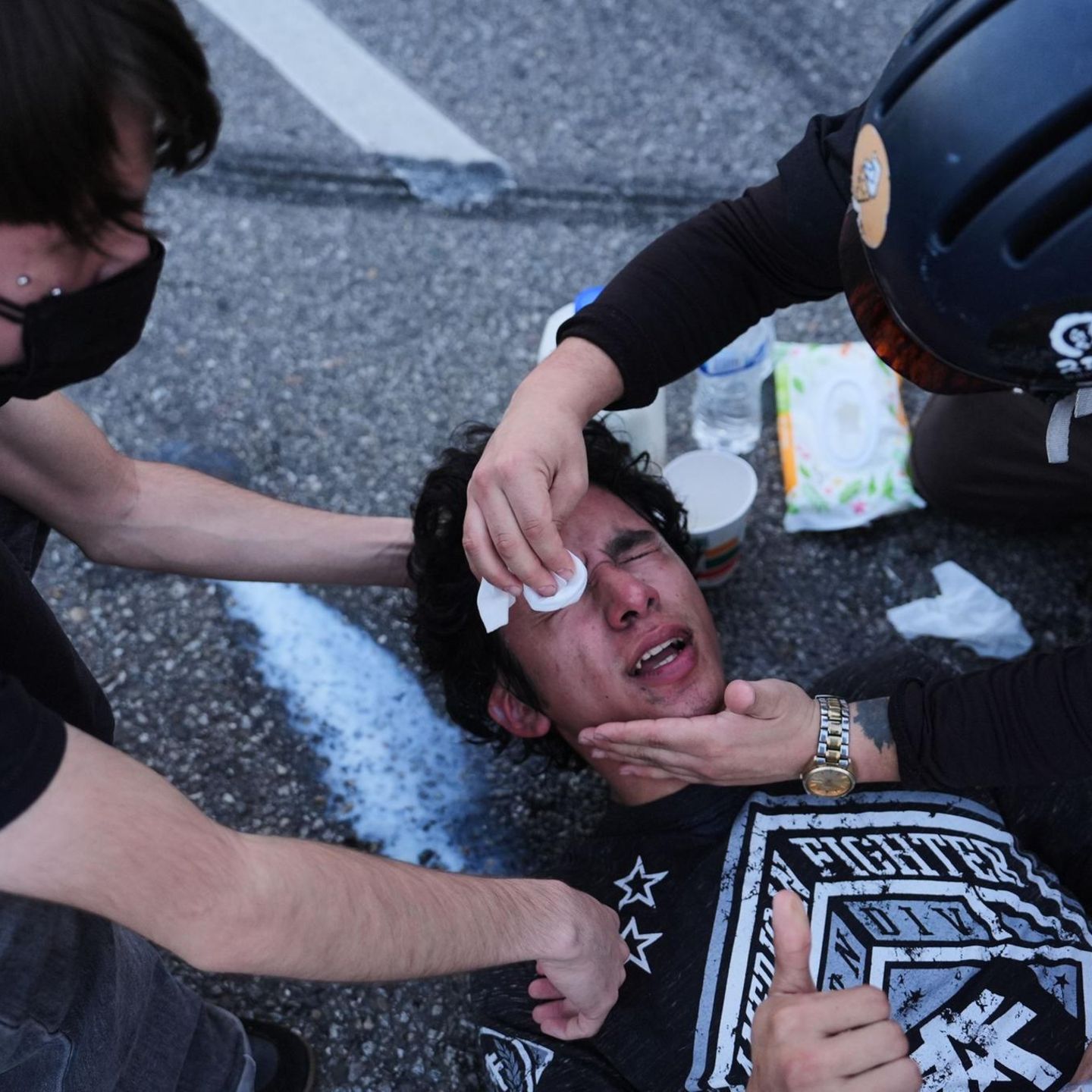 Anti-Ice Demo in den USA: Demonstrant liegt auf Boden, zwei Menschen helfen, ihm seine Augen auszuwaschen