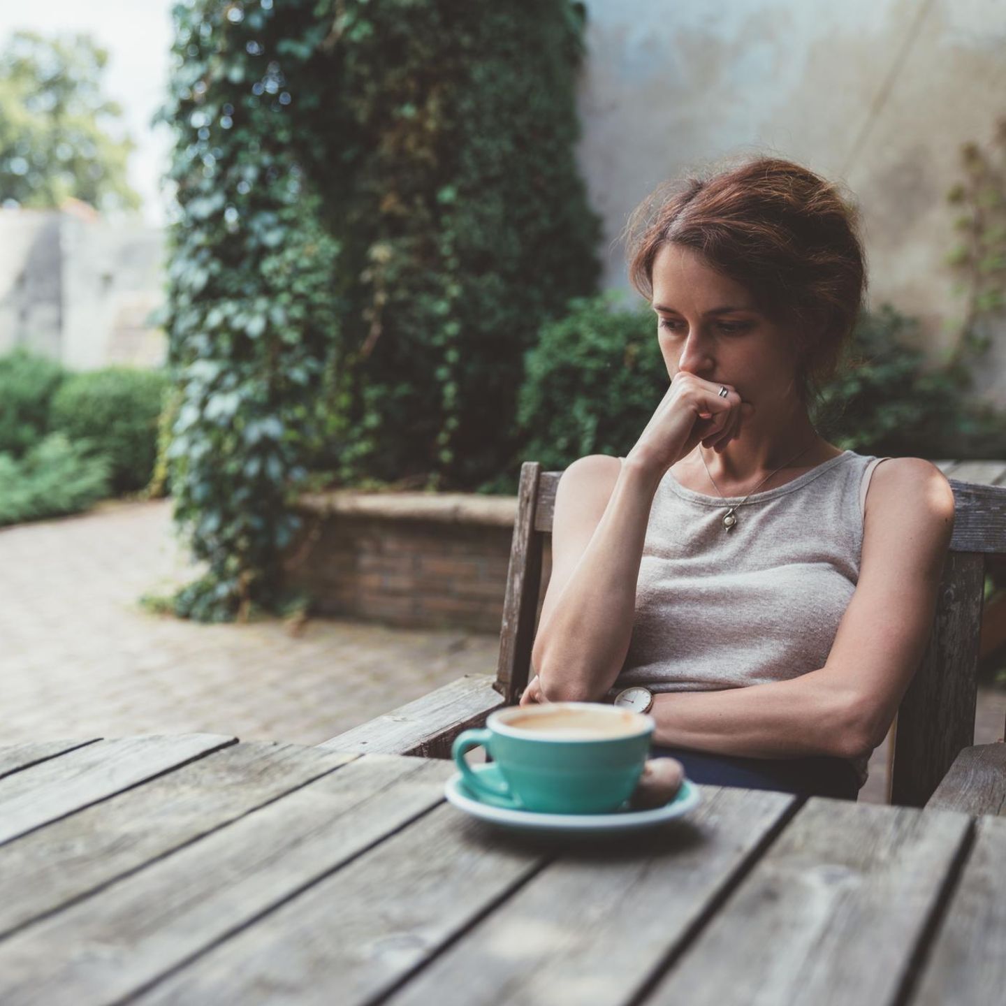 Symbolbild Gebärmutterhalskrebs: Eine Frau sitzt nachdenklich vor ihrem Kaffee auf der Terrasse