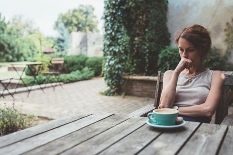 Symbolbild Gebärmutterhalskrebs: Eine Frau sitzt nachdenklich vor ihrem Kaffee auf der Terrasse