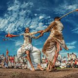 "Die Füße im Matsch, die Herzen im Göttlichen" lautet der ursprüngliche Titel dieses Fotos, das vor Dynamik nur so strotzt. Zwei Männer tanzen mit sichtlicher Freude und messen sich in einem symbolischen Stockkampf. Über der Schulter tragen sie die traditionellen langen Bambusstöcke mit orangefarbenen Fahnen, die im Wind spielen. Ihr Pulikum jubelt und klatscht. Zuschauer und Tanzende gehören zu den "Varkari", einer indischen Religionskultur, deren Anhänger großen Wert auf Gesang und Musik legen