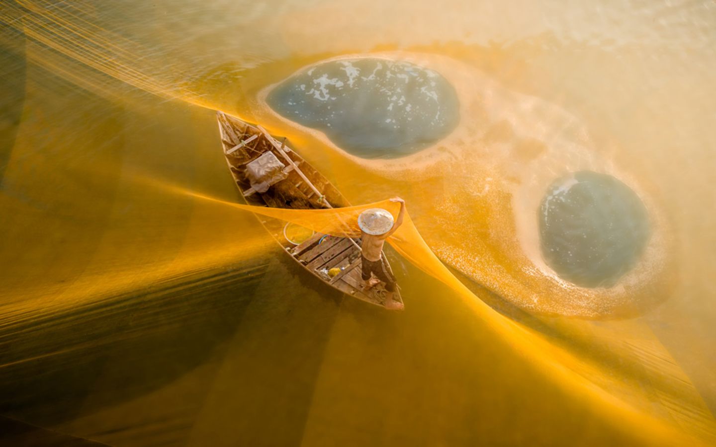 Im Morgenlicht leuchten die Netze golden über einem Fluss in Vietnam. Die Fischer spannen sie für ihren Fang weit übers Wasser. Auf Teo Chin Leongs Foto ist der Fang nicht zu sehen. Die sanften Farben und die klare Komposition lassen die Szene friedlich wirken, fast wie in einem Traum oder einer Fantasie