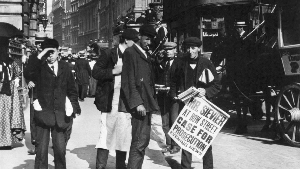 Ein Zeitungsverkäufer steht zwischen Kutschen und Menschen in der Cornhill Street in London (1909)