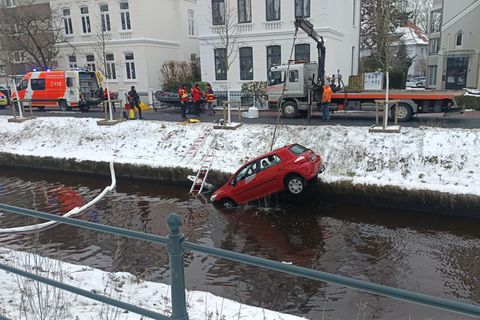 Ein Abschleppwagen mit Kranausleger hebt ein kleines rotes Auto aus einem Fluss in Oldenburg
