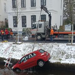 Ein Abschleppwagen mit Kranausleger hebt ein kleines rotes Auto aus einem Fluss in Oldenburg