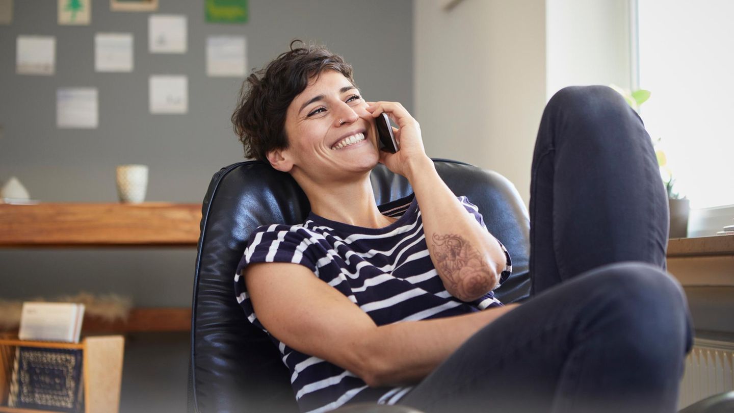 Eine junge Frau sitz in einem Sessel und telefoniert lachend am Smartphone