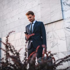 Ein junger Mann mit Aktentasche in der Hand blickt auf sein Handy.