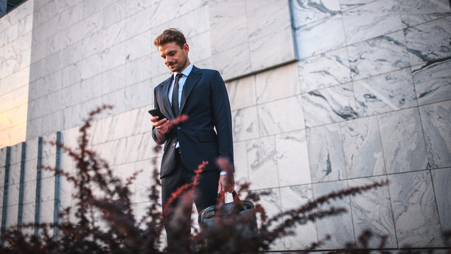 Ein junger Mann mit Aktentasche in der Hand blickt auf sein Handy.