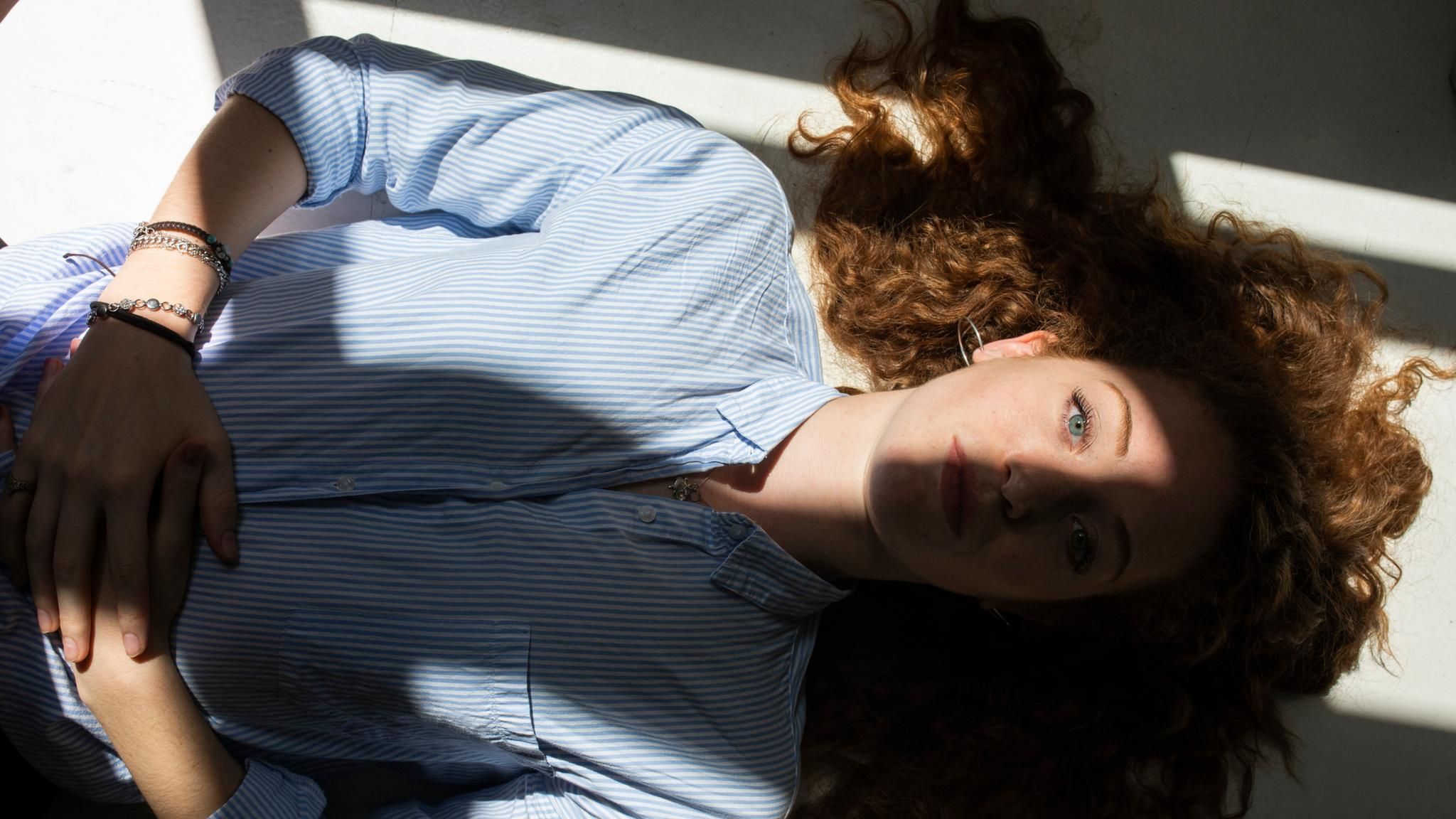 Stress: Eine Frau liegt entspannt auf dem Rücken. Sonne fällt durch ein Fenster auf ihr Gesicht