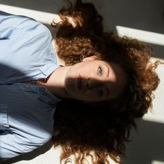 Stress: Eine Frau liegt entspannt auf dem Rücken. Sonne fällt durch ein Fenster auf ihr Gesicht