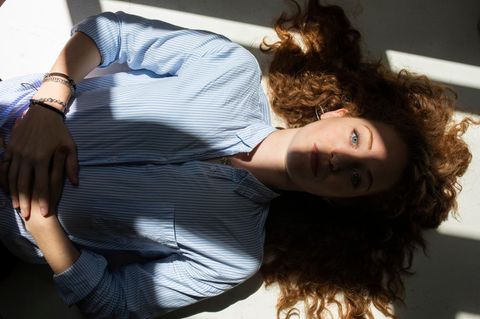 Stress: Eine Frau liegt entspannt auf dem Rücken. Sonne fällt durch ein Fenster auf ihr Gesicht