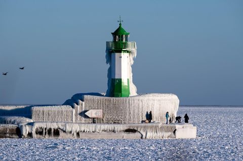 Grün-weißer Leuchtturm in der Ostsee. Lange Eiszapfen bedecken ihn. Die Ostsee ist bis zum Horizont gefroren.