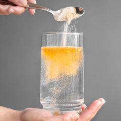 Eine Frau füllt ein Elektrolytpulver in ein Glas mit Wasser