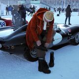 Vor einem Jaguar zieht sich ein Mann Stiefel an