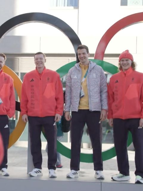 Wintersportler posieren vor den olympischen Ringen.