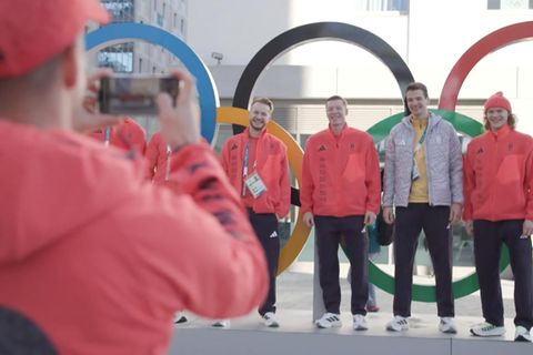 Wintersportler posieren vor den olympischen Ringen.