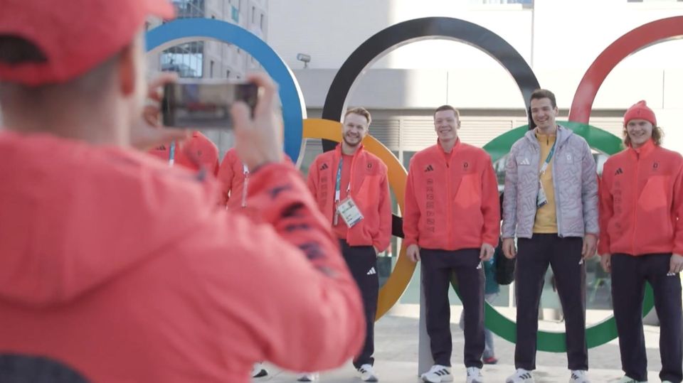 Wintersportler posieren vor den olympischen Ringen.
