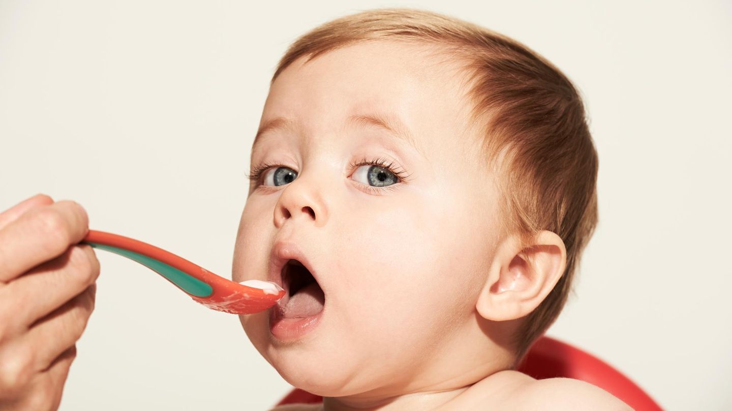 Allergie: Ein Baby öffnet den Mund um einen Löffel mit Brei entgegenzunehmen während es in die Kamera schaut