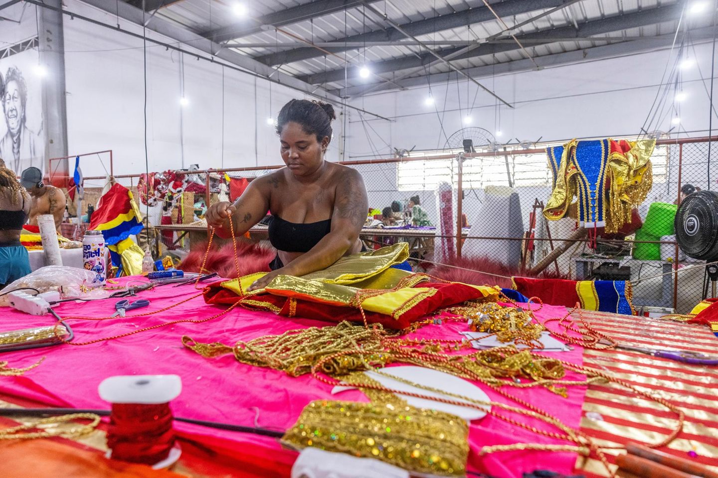 Eine Schneiderin steht vor pinken und goldenen Stoffen
