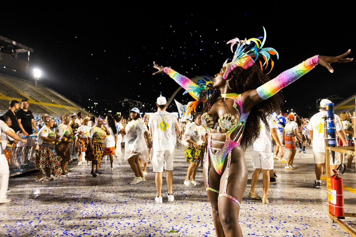 Eine Tänzerin in buntem Kostüm streckt die Arme in die Höhe, hinter ihr weitere Tänzer