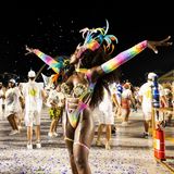 Eine Tänzerin in buntem Kostüm streckt die Arme in die Höhe, hinter ihr weitere Tänzer