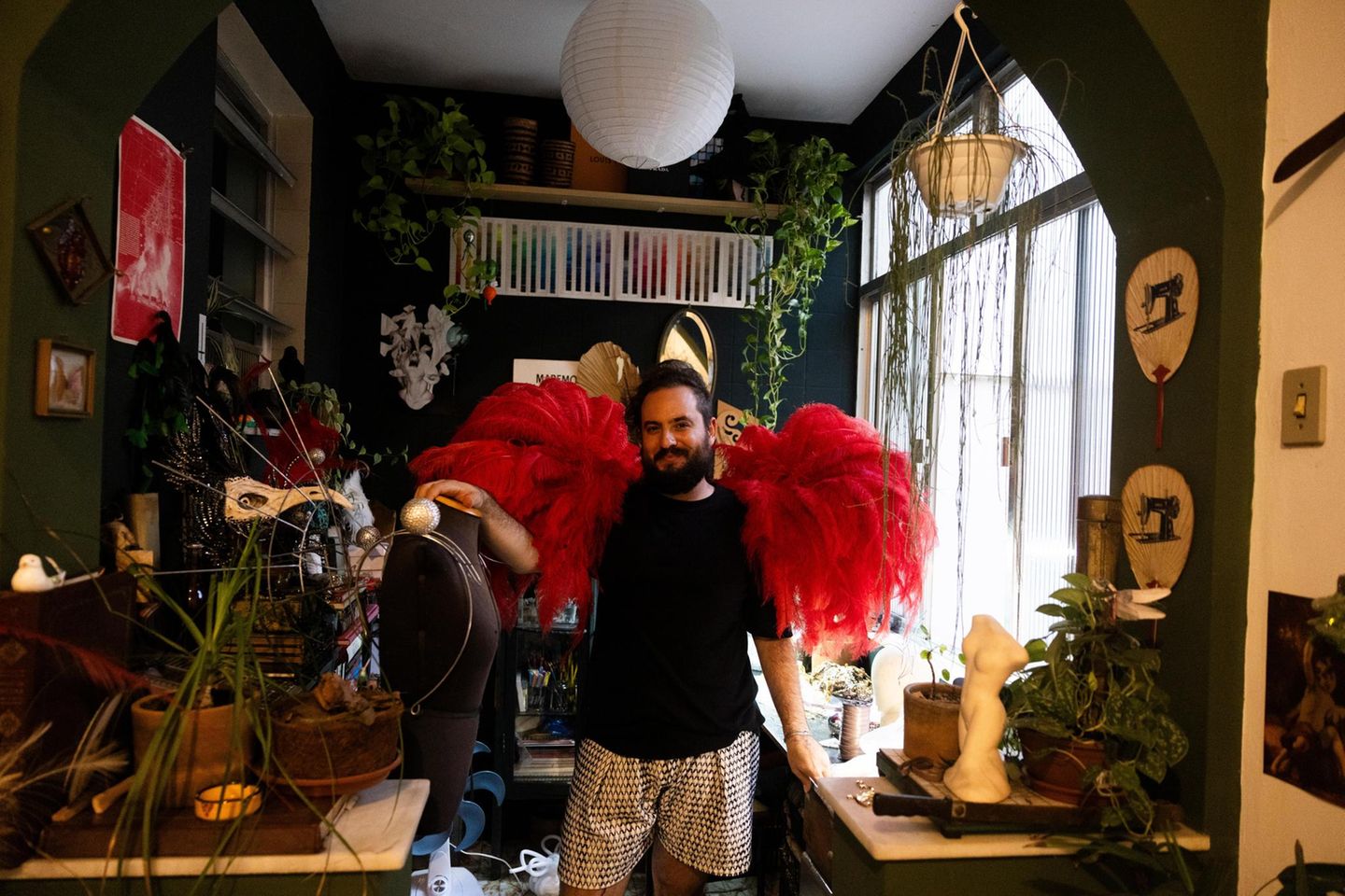 Ein Designer steht in seinem Atelier, er hat eine Federboa um