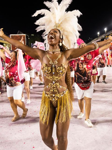 Eine Frau strahlt im Gesicht und streckt die Hände zum Himmel, sie trägt ein aufwendiges Kostüm mit Federschmuck