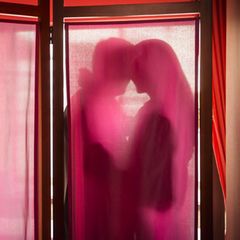 Ein Paar hinter einem Vorhang (Symbolbild Sugarbabe mit Sugardaddy)