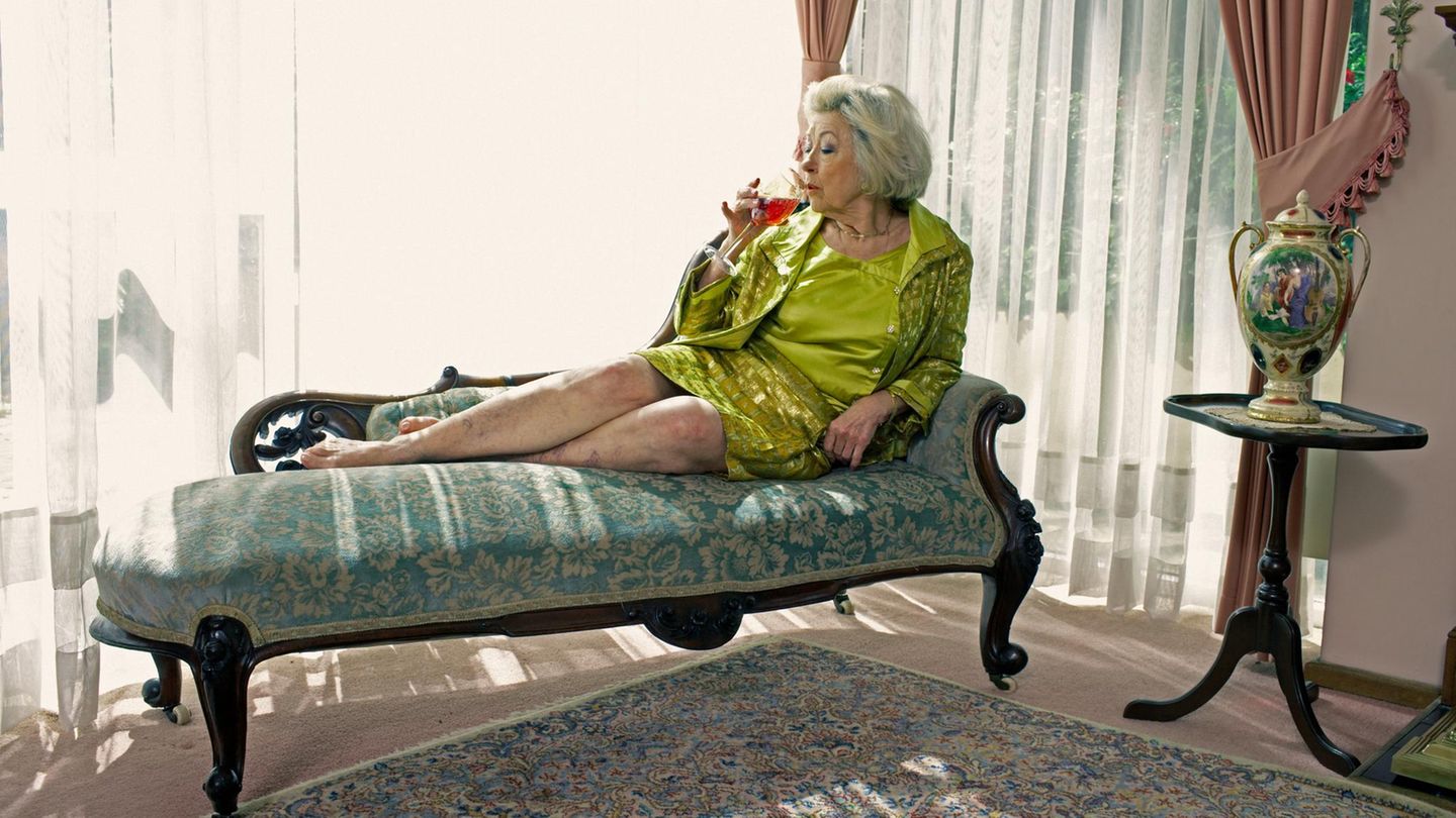 Eine alte Frau liegt auf einem Recamee und trinkt Wein (Symbolbild Eltern trinken)