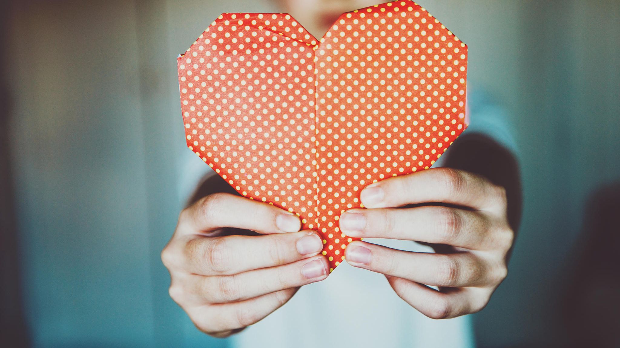 Ein KInd hält ein rotes Origami Herz hoch