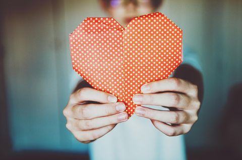 Ein KInd hält ein rotes Origami Herz hoch