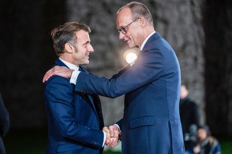 Merz und Macron schütteln die Hände, Merz legt Macron die linke auf die Schulter