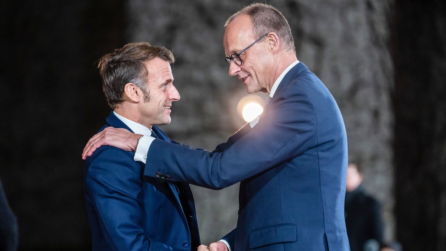 Merz und Macron schütteln die Hände, Merz legt Macron die linke auf die Schulter