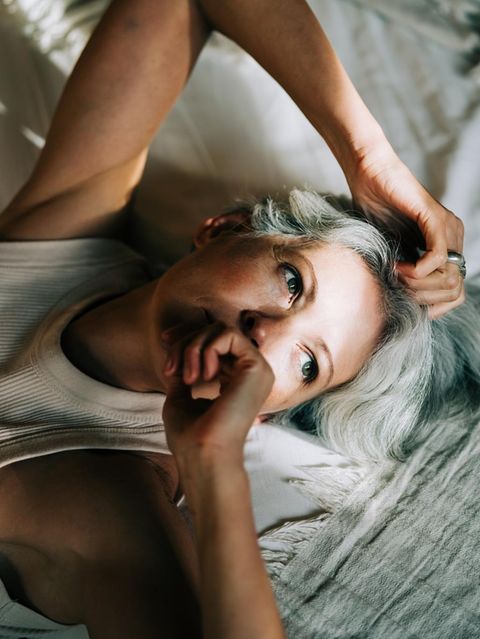 Eine Frau mit grauen Haaren liegt auf einem Bett und schaut nachdenklich (Symbolbild ADHS bei Frauen)