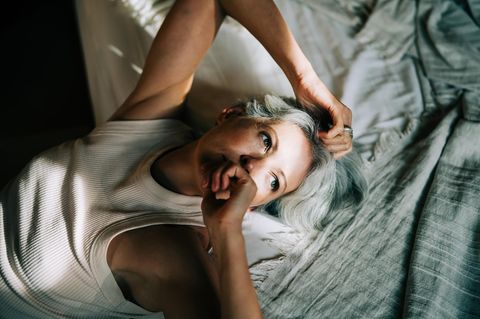 Eine Frau mit grauen Haaren liegt auf einem Bett und schaut nachdenklich (Symbolbild ADHS bei Frauen)