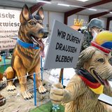 Motivwagen: Wiese mit aggressiven Hunden mit AfD-Halsband, Hund mit Karnevalshut und Schild "Wir dürfen draußen bleiben" davor