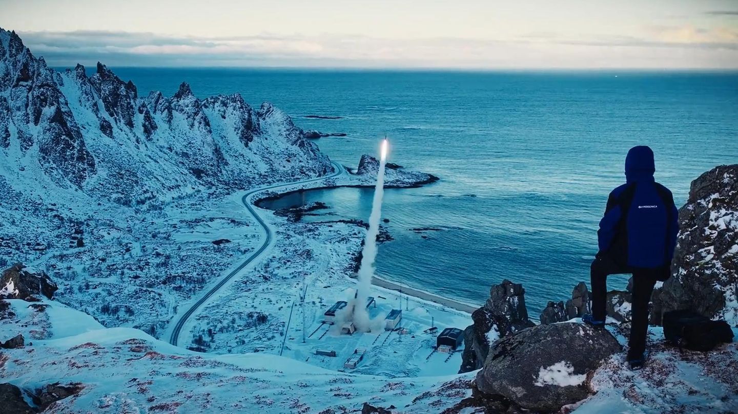 Ein Mann steht auf einem Berg und beobachtete den Start einer Rakete im Tal