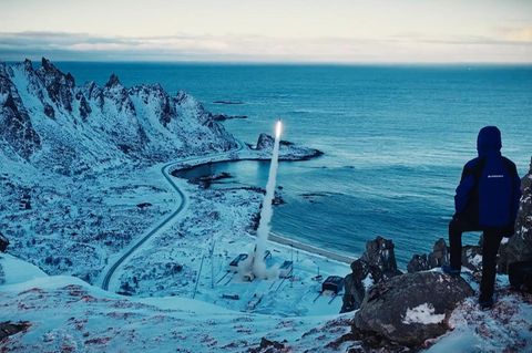 Ein Mann steht auf einem Berg und beobachtete den Start einer Rakete im Tal