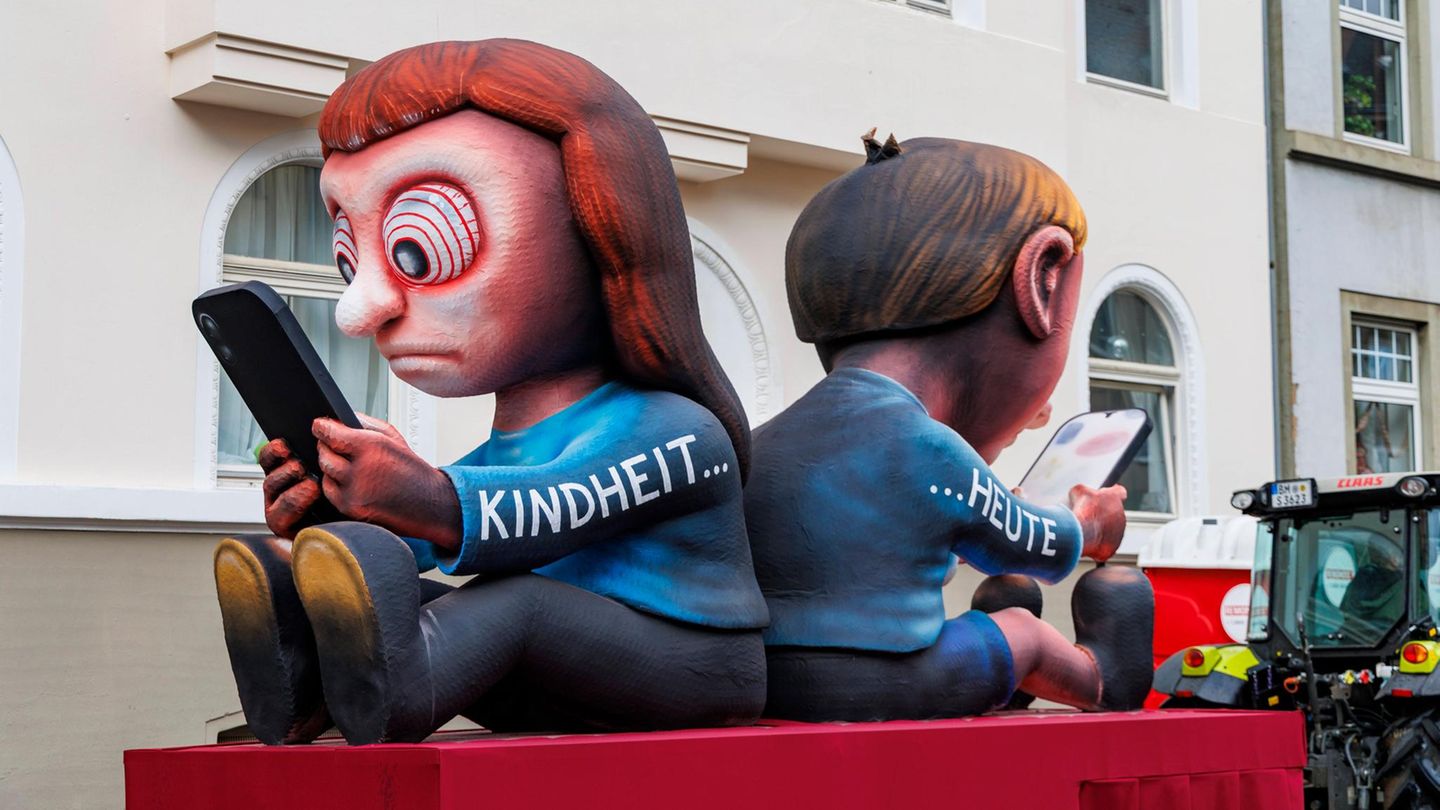 „Kindheit … heute“: Hypnotisiert vom Smartphone starren zwei Kinder auf die Bildschirme in ihren Händen. Aktuell läuft weltweit die Debatte darüber, Handynutzung für Kinder per Gesetz einzuschränken: Ein Social-Media-Verbot für Jugendliche hat Australien etwa durchgesetzt.