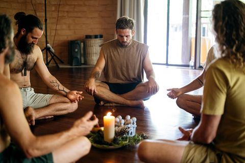 Mann sitzt mit anderen in einem Kreis und meditiert konzentriert (Symbolbild Buddhismus)