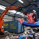 Ein Bagger hebt eine Pappfigur eines Rosenmontagszügen in den Müll