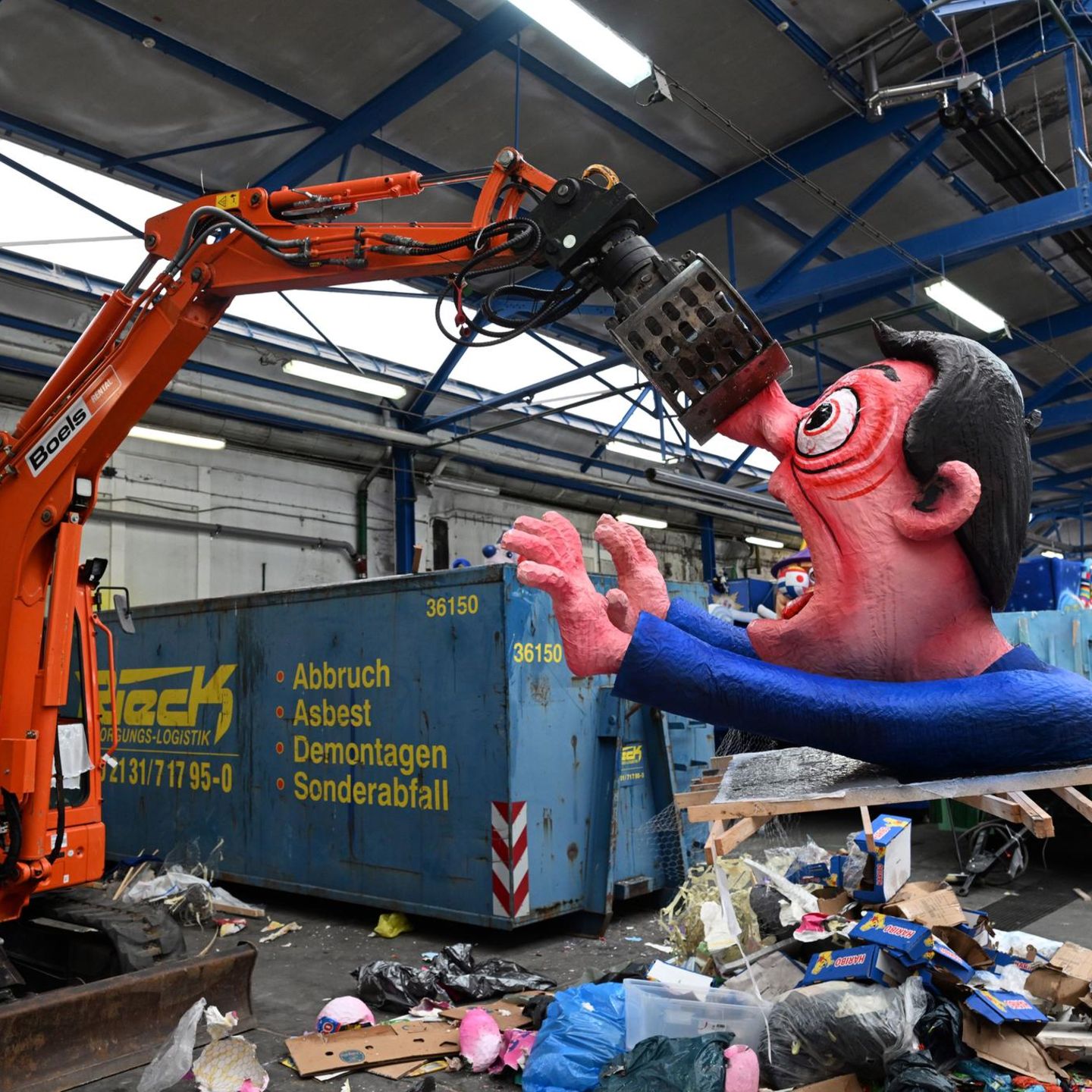 Ein Bagger hebt eine Pappfigur eines Rosenmontagszügen in den Müll