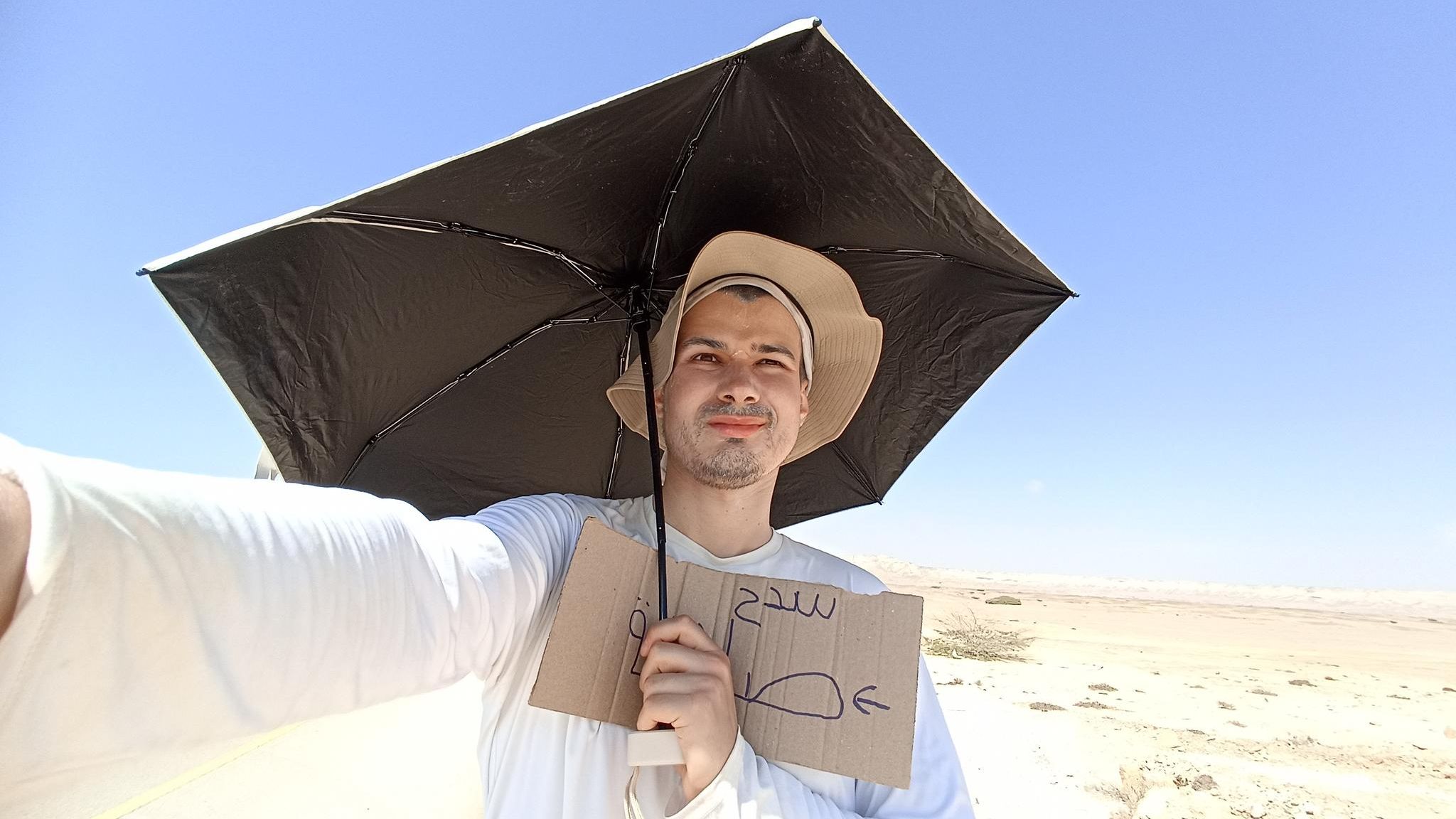 Lukas Stock beim Warten auf ein Auto mit Sonnensegel, Hut und Schild