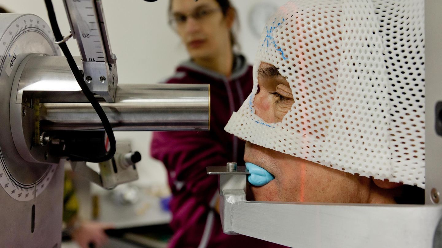 Krebs im Auge – das Aderhautmelanom  Augenkrebs ist insgesamt selten, das Aderhautmelanom die häufigste, aber dennoch extrem seltene bösartige Form. Der Tumor entsteht aus Pigmentzellen in der Aderhaut des Auges und bleibt lange unbemerkt. Frühe Symptome fehlen häufig, später können Sehstörungen, Schatten im Gesichtsfeld oder Lichtblitze auftreten. Der biologische Grund für die Seltenheit liegt in der Anatomie des Auges: Die Zahl der Melanozyten ist gering, ihre Teilungsrate niedrig. Zudem ist das Auge ein sogenanntes immunprivilegiertes Organ mit besonderen Schutzmechanismen. All das macht bösartige Entartungen selten – aber diagnostisch besonders tückisch.  Das Bild zeigt einen Mann bei der Protonentherapie an der Berliner Charité. Diese hochpräzise, augenerhaltende Behandlungsmethode für Aderhautmelanome ermöglicht die gezielte Zerstörung des Tumors bei hoher Schonung des umliegenden Gewebes und des Sehnervs. 