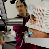 Krebs im Auge – das Aderhautmelanom  Augenkrebs ist insgesamt selten, das Aderhautmelanom die häufigste, aber dennoch extrem seltene bösartige Form. Der Tumor entsteht aus Pigmentzellen in der Aderhaut des Auges und bleibt lange unbemerkt. Frühe Symptome fehlen häufig, später können Sehstörungen, Schatten im Gesichtsfeld oder Lichtblitze auftreten. Der biologische Grund für die Seltenheit liegt in der Anatomie des Auges: Die Zahl der Melanozyten ist gering, ihre Teilungsrate niedrig. Zudem ist das Auge ein sogenanntes immunprivilegiertes Organ mit besonderen Schutzmechanismen. All das macht bösartige Entartungen selten – aber diagnostisch besonders tückisch.  Das Bild zeigt einen Mann bei der Protonentherapie an der Berliner Charité. Diese hochpräzise, augenerhaltende Behandlungsmethode für Aderhautmelanome ermöglicht die gezielte Zerstörung des Tumors bei hoher Schonung des umliegenden Gewebes und des Sehnervs. 