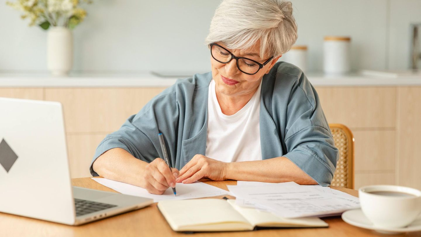 Rente und Steuern: Eine ältere Frau sitzt an einem Tisch und schreibt etwas auf