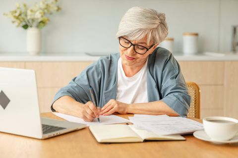 Rente und Steuern: Eine ältere Frau sitzt an einem Tisch und schreibt etwas auf
